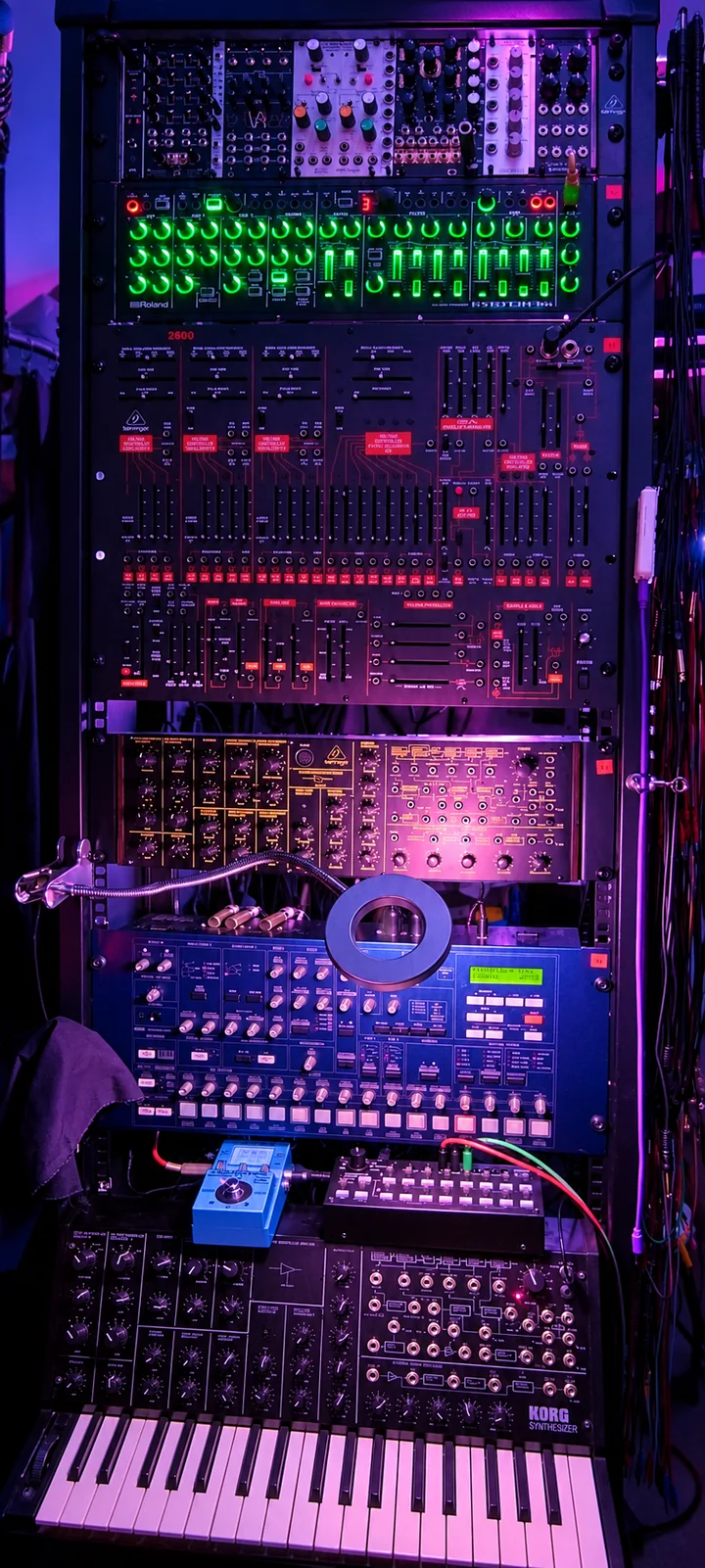 Rack vertical de synthétiseurs, éclairé en bleu et violet, avec ses commandes lumineuses vertes
